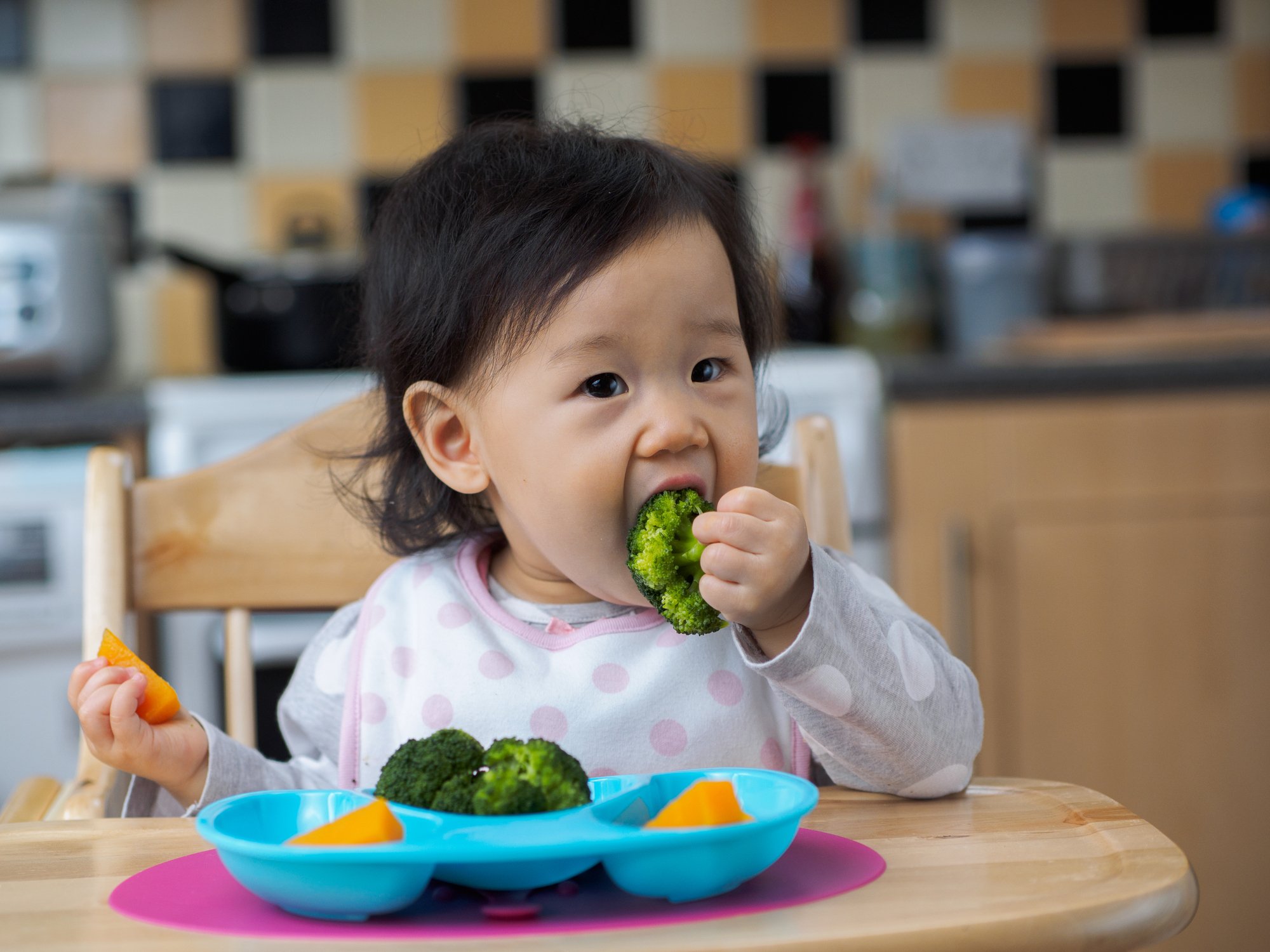 Asian baby girl eating vegetable first time at home kitchen