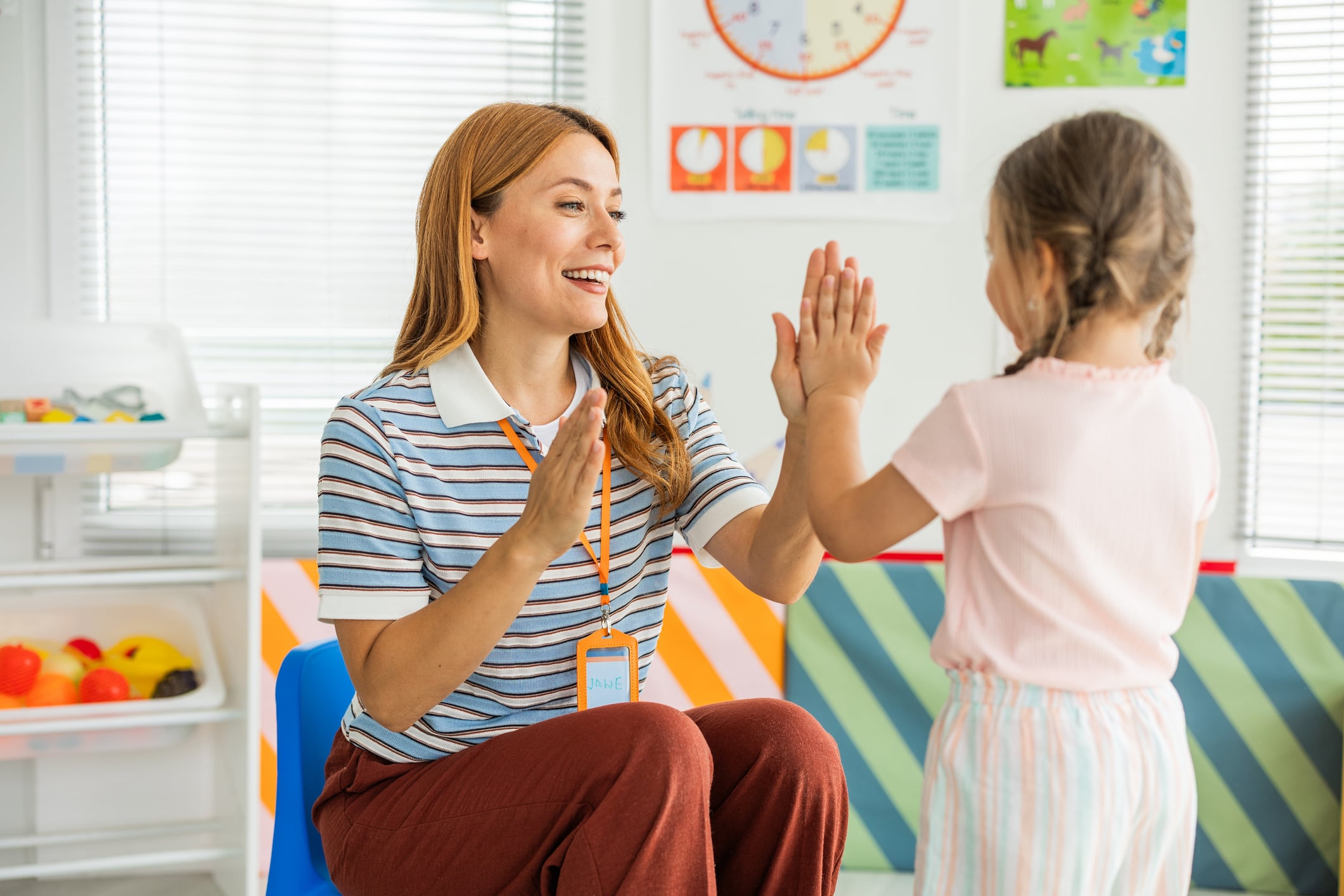 Smiling teacher playing with little girl at kindergarten